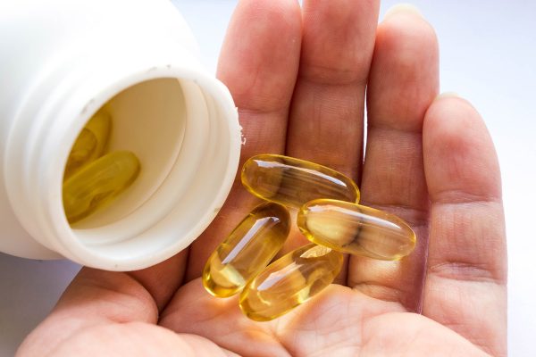 Taking food supplements and vitamins. A white jar of fish oil in jelly-like transparent yellow capsules and a handful of capsules in a woman's palm close-up on a white background.